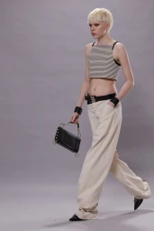 Model with blonde hair walking on a grey seamless background wearing a striped crop top and wide-leg trousers