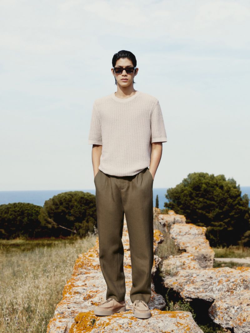 Portrait of a young adult man in casual short-sleeve shirt, pants and sunglasses, posing outdoors with natural light and sky.
