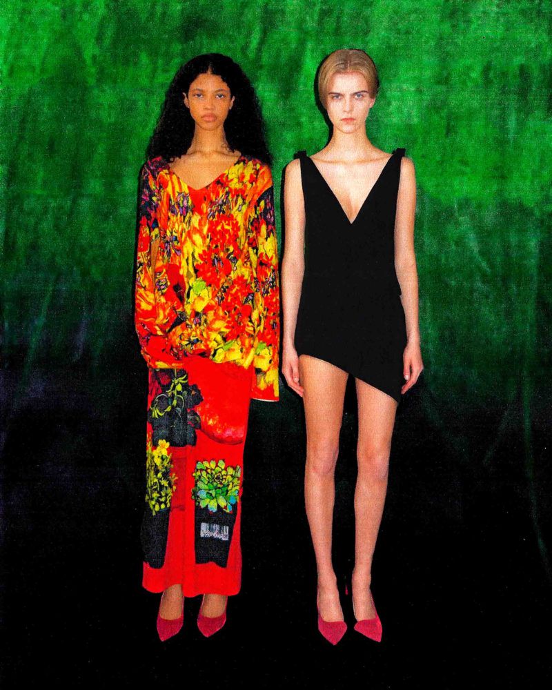 Two women in stylish dresses and pink heels pose against a vibrant green and black backdrop, creating a bold fashion statement.