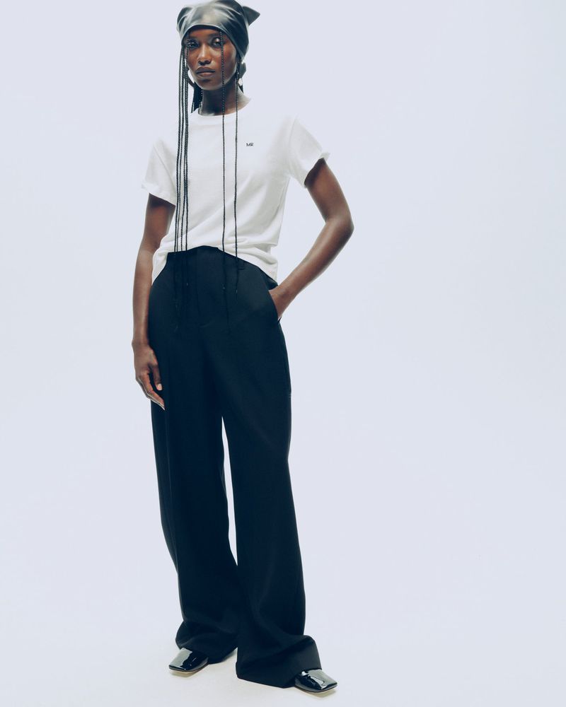 Fashion shot of a Black model wearing a white t-shirt, black pants, and a black leather headscarf, posing in a bright photo studio.