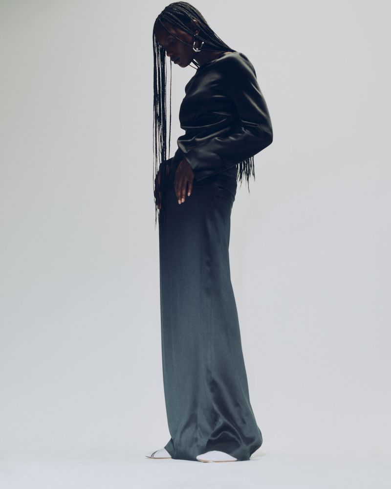 Elegant Black Woman Posing in Satin Dress: A sophisticated image featuring a woman in a long black satin dress against a light background.