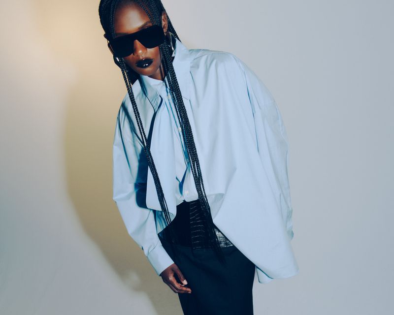 Fashionable woman in oversized shirt and sunglasses. Stylish studio shot of an African woman with braided hair and dark lipstick.