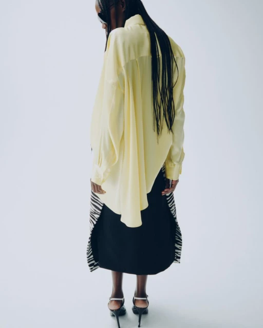 Back view of an adult woman in a yellow blouse, black skirt with a zebra-print hem, and heels against a clean white backdrop.