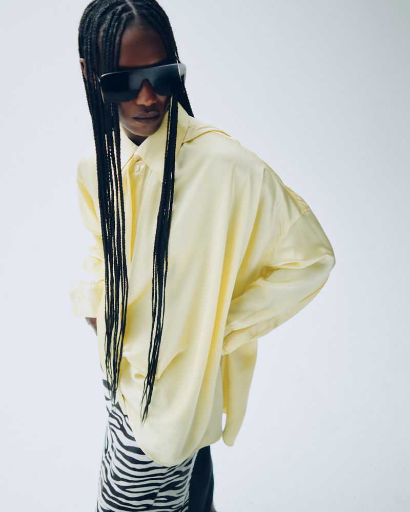 Fashionable adult female wearing oversized pale-yellow shirt, black sunglasses and zebra print skirt in a studio setting.