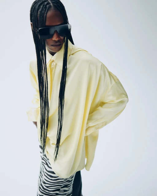 Fashionable adult female wearing oversized pale-yellow shirt, black sunglasses and zebra print skirt in a studio setting.