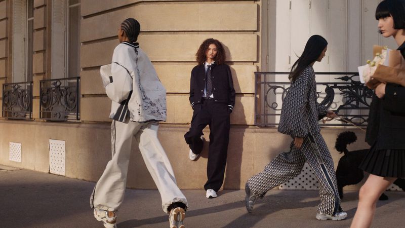 Fashion editorial featuring several adult women walking on a city sidewalk wearing stylish outfits; Parisian architecture in the background.