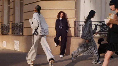 Four models walking and posing on a sunlit city street past a classical stone building for Dior Chrono sneakers campaign by Sarah Blais.