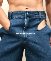 Close-up shot of a person wearing blue denim cutout trousers with one hand in a pocket and a bare torso.