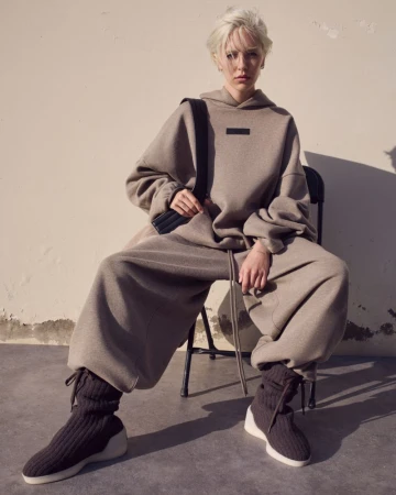Model Delilah Belle seated wearing an oversized taupe fleece hoodie and sweatpants set with dark knit boots for Fear of God.