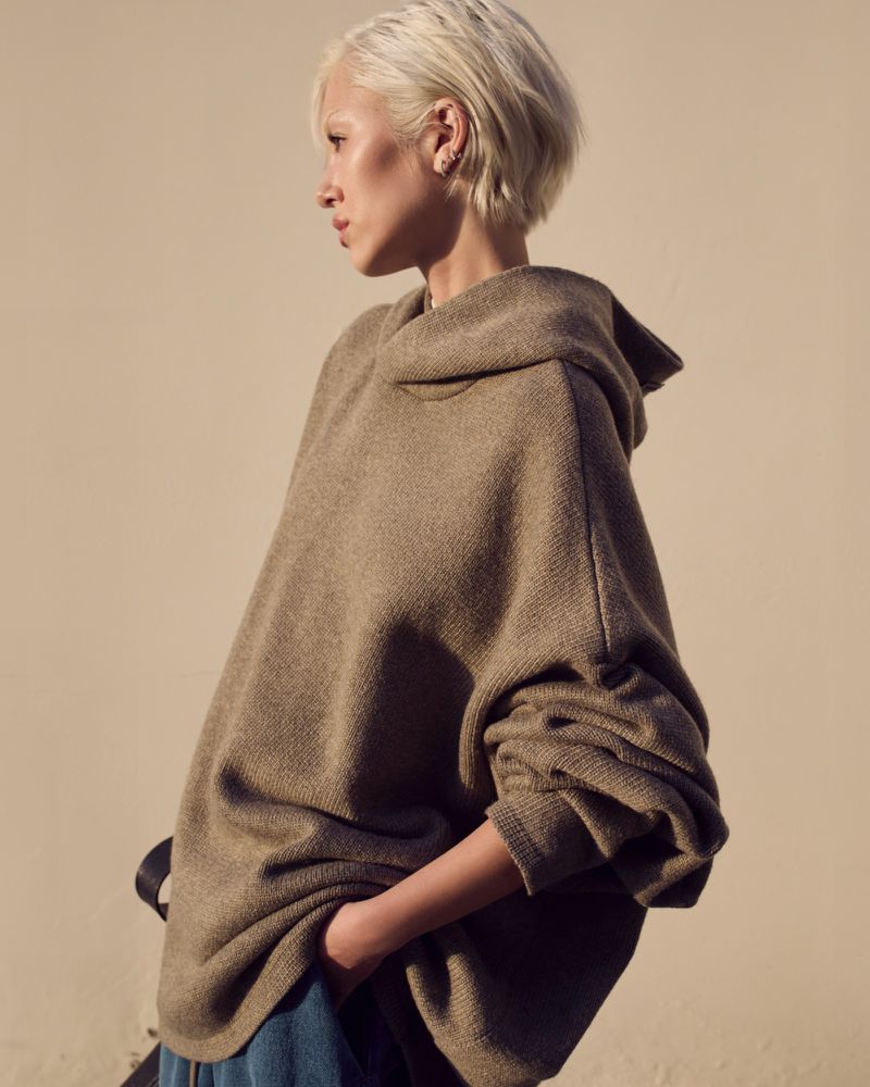 Woman in oversized hoodie poses in a medium shot. Neutral background, soft lighting. Fashion, lifestyle photography.