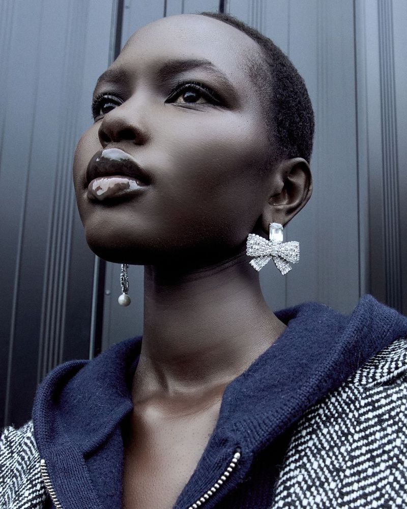 Close-up shot of a fashionable Black woman wearing large, shiny, bow-shaped earrings and a wool jacket. Her dark skin tone stands out.