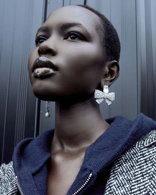 Close-up shot of a fashionable Black woman wearing large, shiny, bow-shaped earrings and a wool jacket. Her dark skin tone stands out.