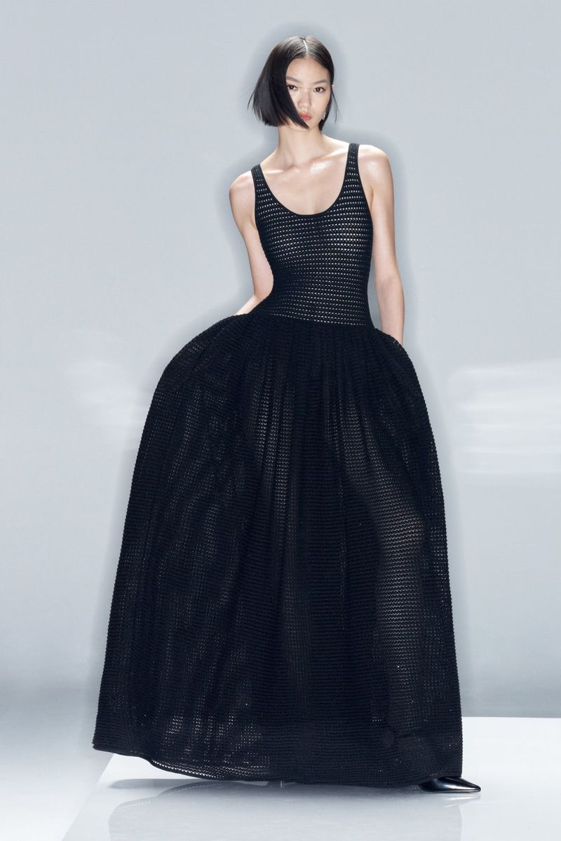 Fashion shoot featuring a lone Asian female model wearing a black evening gown with a tulle skirt, shot in a bright studio.
