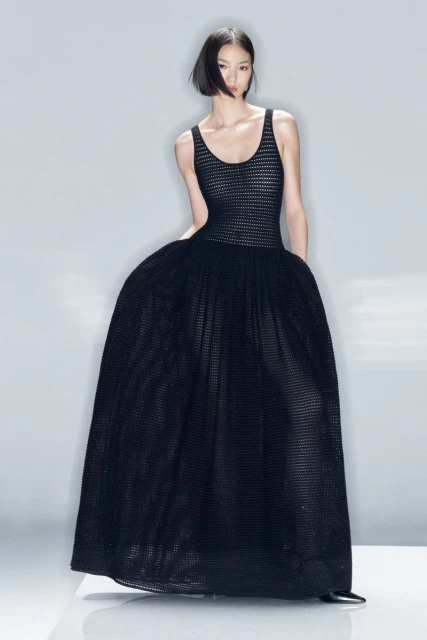 Fashion shoot featuring a lone Asian female model wearing a black evening gown with a tulle skirt, shot in a bright studio.