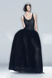 Model Huijia Chen poses in a sleeveless black voluminous full-skirt gown against a light grey studio background.