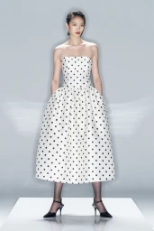 Model wearing a strapless polka dot dress and black heels on a white studio backdrop for Self-Portrait.