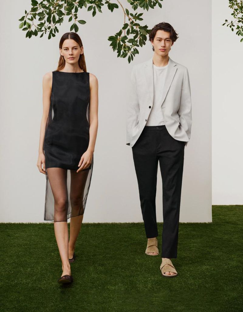 A stylish fashion shoot features a woman in a black dress and a man in a suit, set against a green lawn and decorated with hanging foliage.