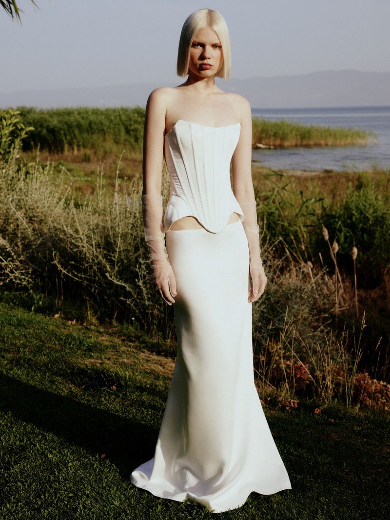 Model with blonde bob wearing a white strapless corset dress outdoors near a body of water for Sudietuz S/S 24 Collection.