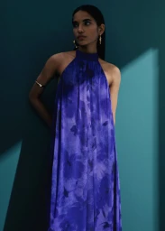 Model in blue halterneck dress standing against a dark teal wall for Mango Adha Collection campaign