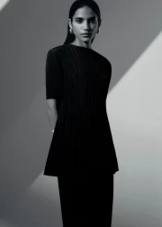 Model in a black pleated top wearing hoop earrings against a geometric grey studio backdrop