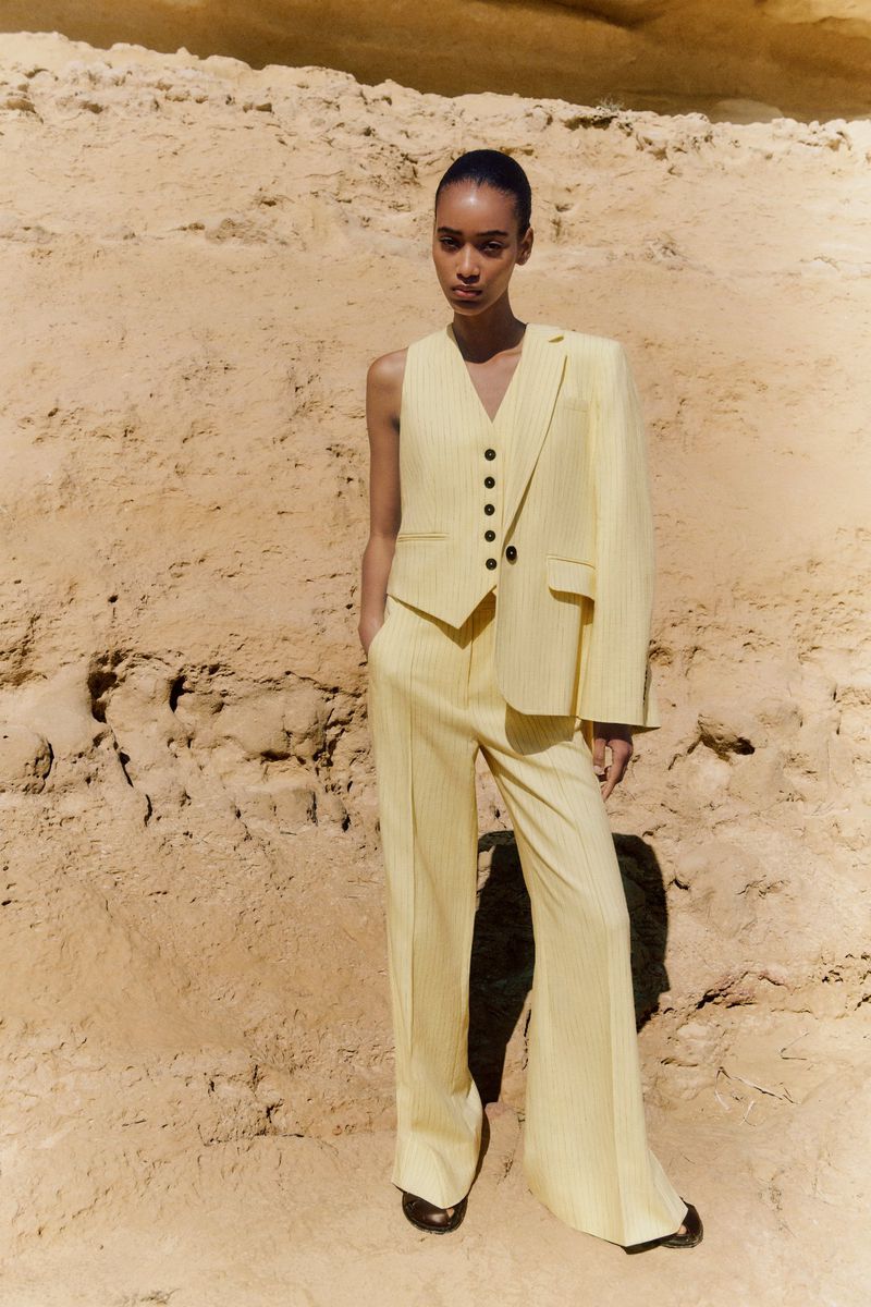Fashion shot of a slender woman posing in a yellow striped suit on a sand dune, highlighting the outfit and the natural environment.