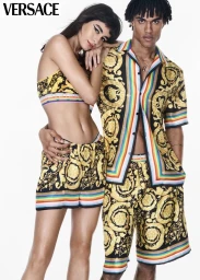 Two models posing in matching yellow and black Versace Barocco print outfits with rainbow stripes against a white background.