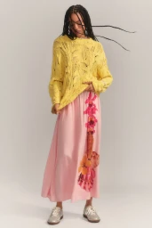 Model in a yellow knit sweater and printed pink maxi skirt with silver sneakers standing against a neutral studio backdrop.