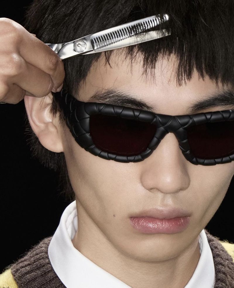 Close-up of a person wearing sunglasses getting a haircut with thinning shears, captured in a studio against a black backdrop.