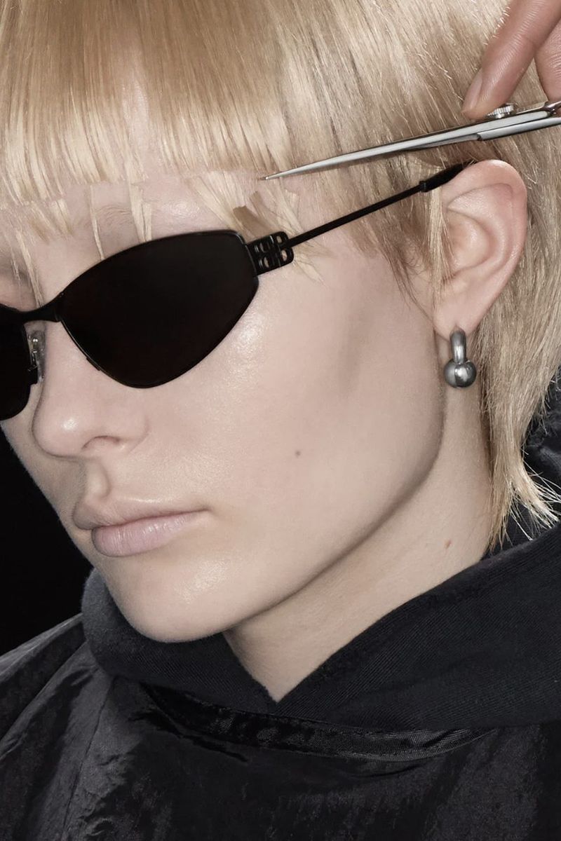 Woman with sunglasses getting a haircut. Close-up of face, hairstyle, and scissor cutting bangs with dark background. Fashion, beauty, style.