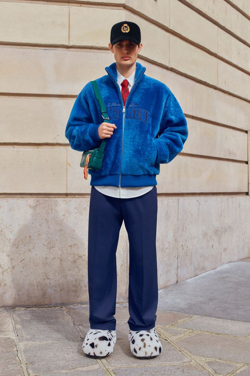 Fashion portrait of a young adult man in a blue sherpa jacket, navy pants, baseball cap, and Dalmatian print shoes, outdoors.