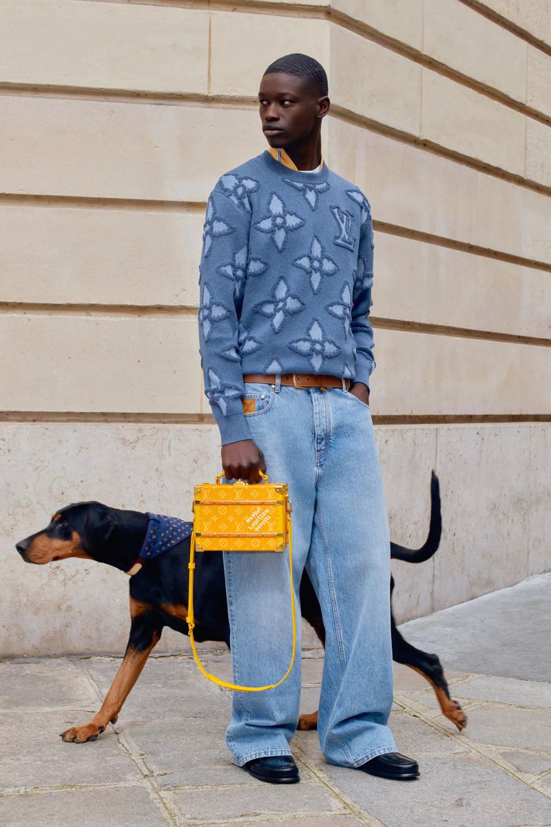 An African American male model poses with a Doberman wearing a patterned bandana and a yellow handbag in an urban setting.