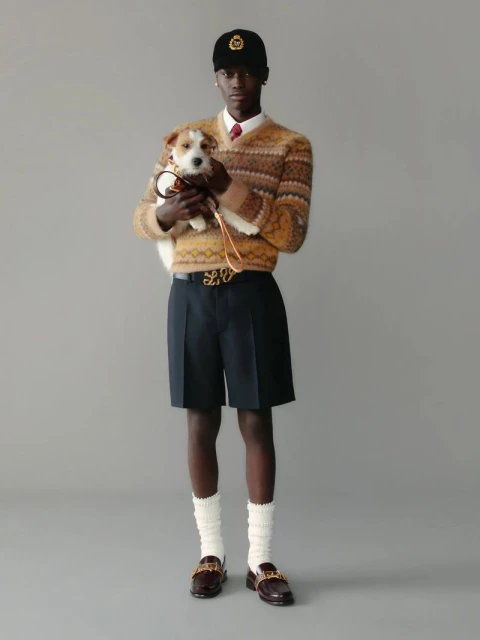 An adult male is holding a small dog in a full shot. The man is wearing a sweater and hat, while the dog is on a leash.