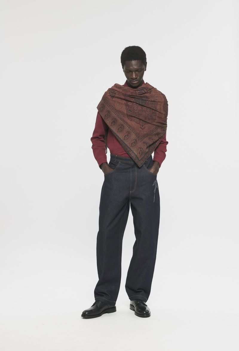 Model Modu Fall wearing a patterned brown shawl, red top, and dark wide-leg jeans against a plain studio background.