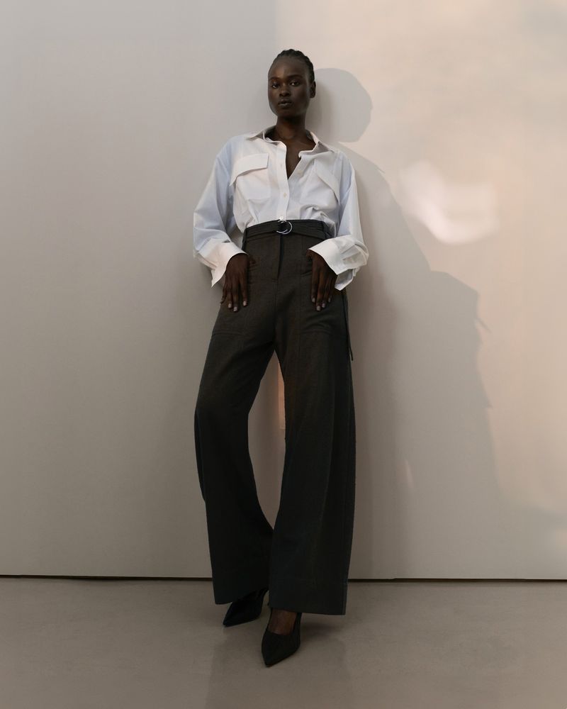 Model Bakhita Lual wearing a white button-down shirt and dark trousers against a minimalist wall for Eudon Choi