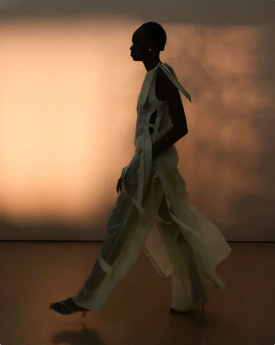 Model silhouetted in profile walking against a softly illuminated gradient background for Eudon Choi SS25 lookbook
