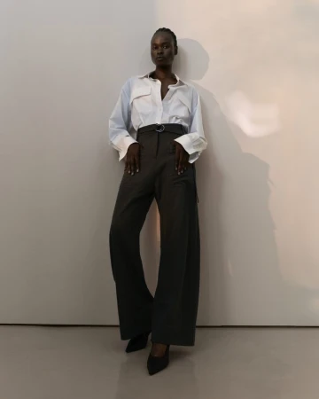 Model Bakhita Lual wearing a white button-down shirt and dark trousers against a minimalist wall for Eudon Choi