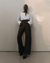 Model Bakhita Lual wearing a white button-down shirt and dark trousers against a minimalist wall for Eudon Choi