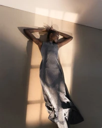 Model lying on the floor under warm light wearing a dark sleeveless dress for Eudon Choi SS25 Lookbook