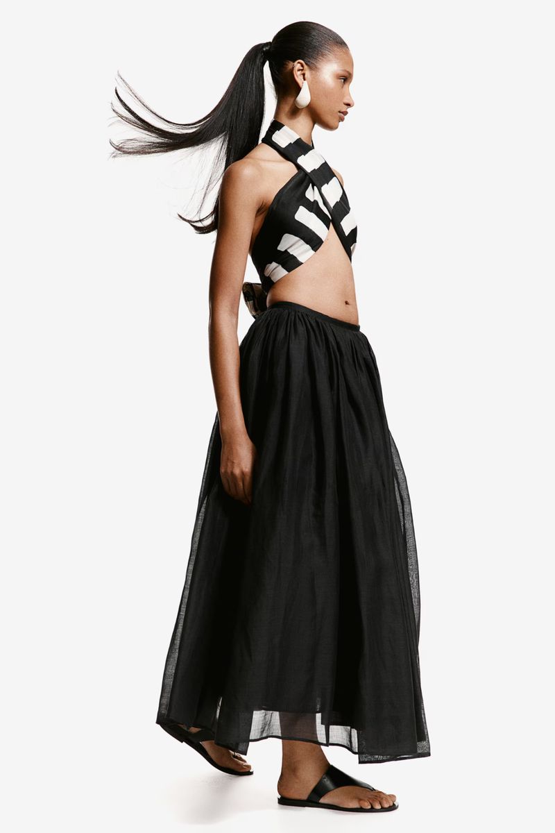 Elegant adult woman in a striped halter top and long black skirt poses in a light studio. Fashion shot featuring the model in profile.