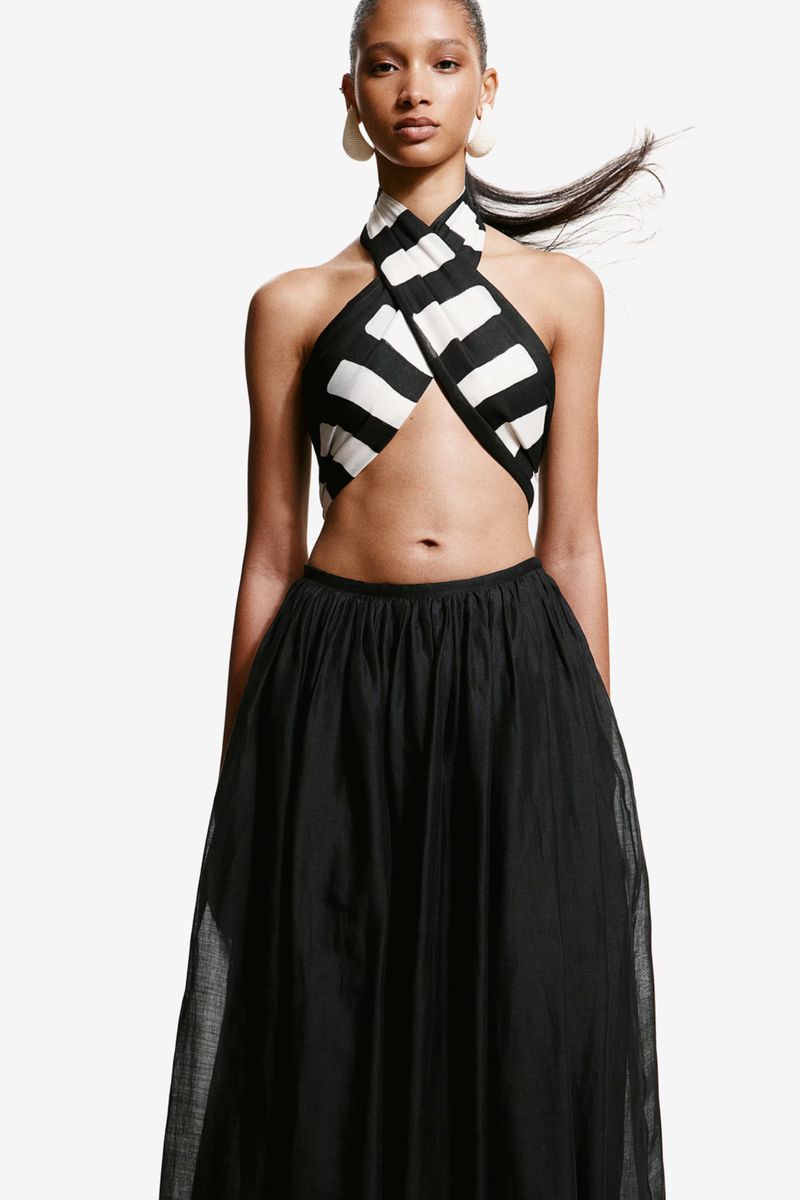 Fashion shot of a woman wearing a black and white striped crop top with a full, long black skirt against a white background.
