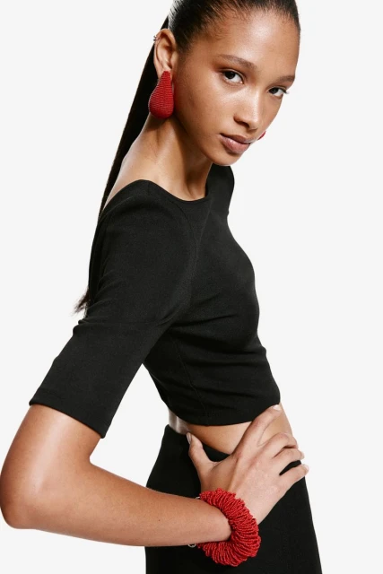 Headshot of woman in black crop top and skirt posing with red bead jewelry against a white backdrop, fashion, studio lighting.