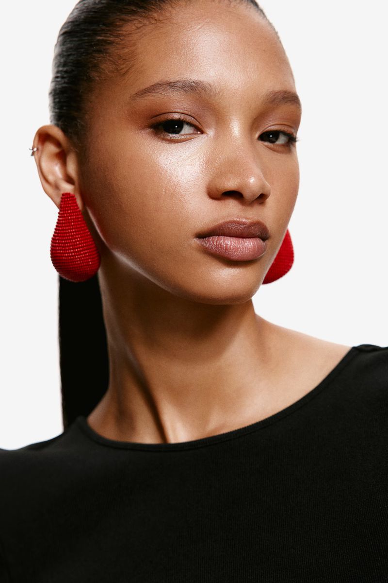 Portrait of a beautiful adult female wearing red teardrop earrings, styled with a black low-cut top, against a clean white backdrop.