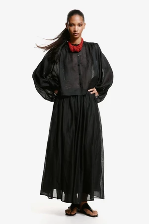 Model in a long black dress and red beaded necklace posing against a clean white background for H&M.