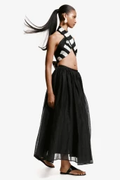 Model Maty Fall posing in profile wearing a black and white halter crop top and sheer black maxi skirt against a white backdrop.