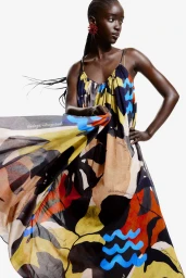 Model wearing a vibrant printed slip dress with a flowing skirt against a plain white background