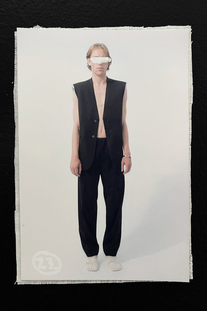 Fashion shot of androgynous person in black vest and pants posing in front of a white background inside a photo studio on canvas.