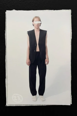 Fashion shot of androgynous person in black vest and pants posing in front of a white background inside a photo studio on canvas.