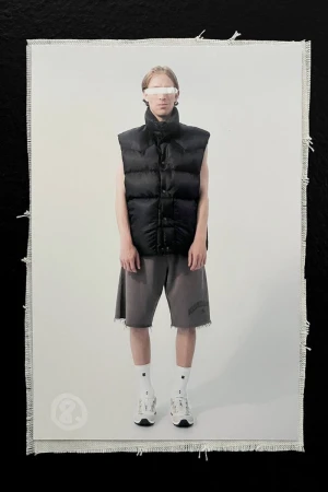 Studio shot of a person wearing a black puffer vest, gray shorts, white socks, and white sneakers, against a white background.