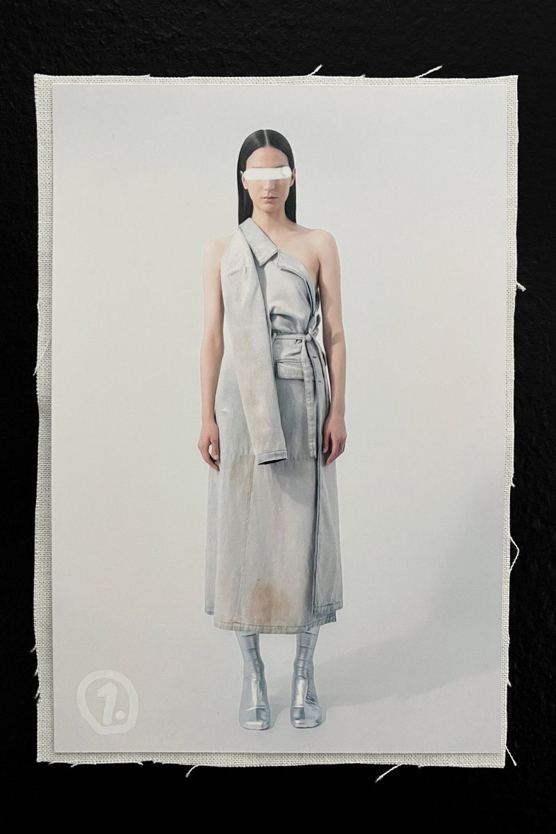 Fashion shot of a woman wearing a light blue dress, metallic boots, and a silver visor against a light gray background on fabric.