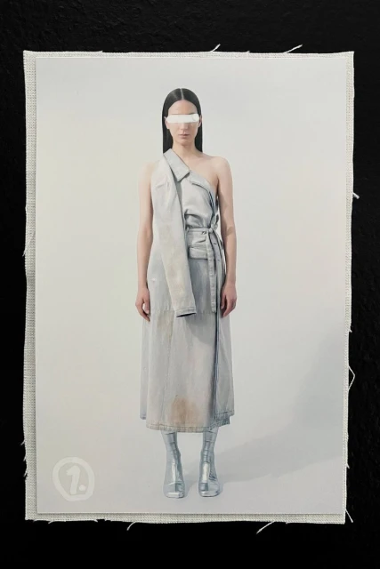 Fashion shot of a woman wearing a light blue dress, metallic boots, and a silver visor against a light gray background on fabric.